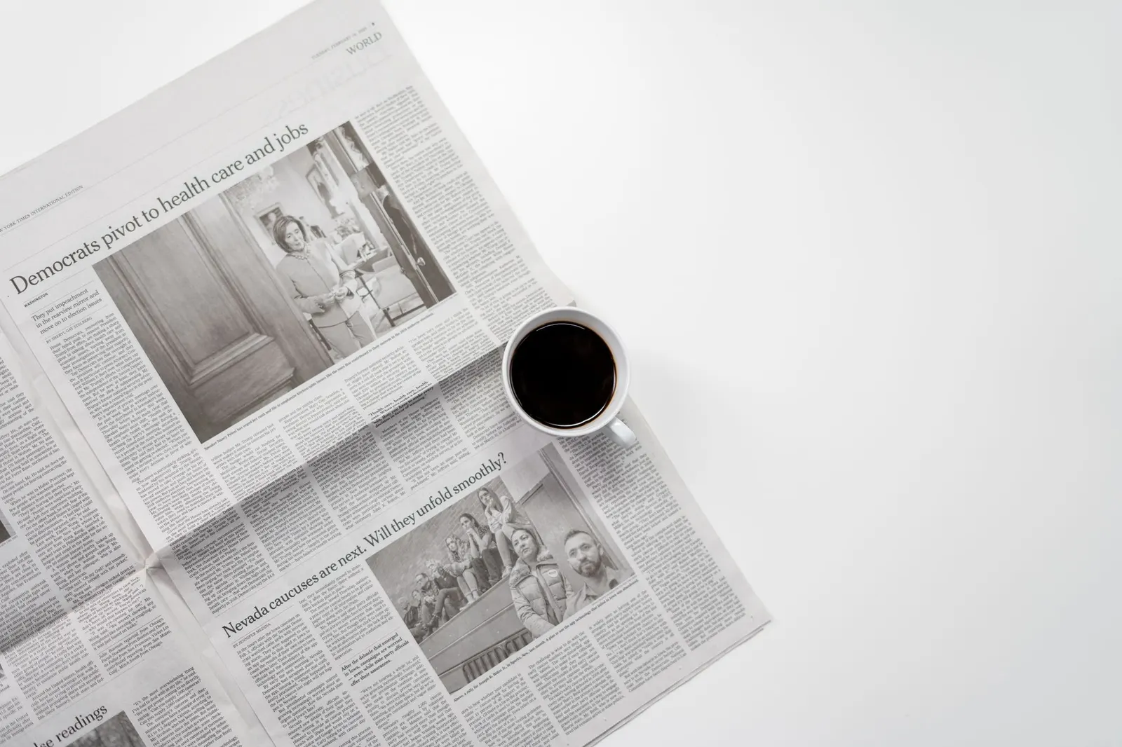 Aufgeschlagene Tageszeitung neben einer Tasse schwarzem Kaffee auf einem weißen Tisch