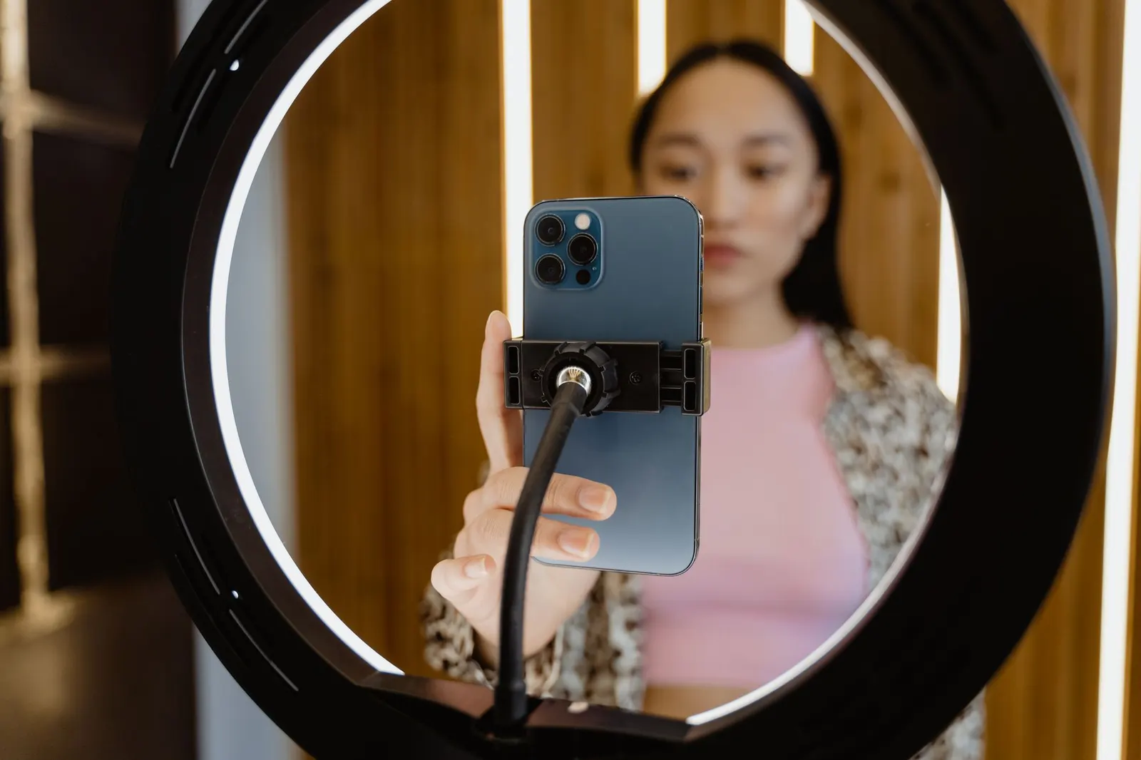 Junge Frau filmt sich mit einem Smartphone, das in der Mitte eines Ringlichts befestigt ist