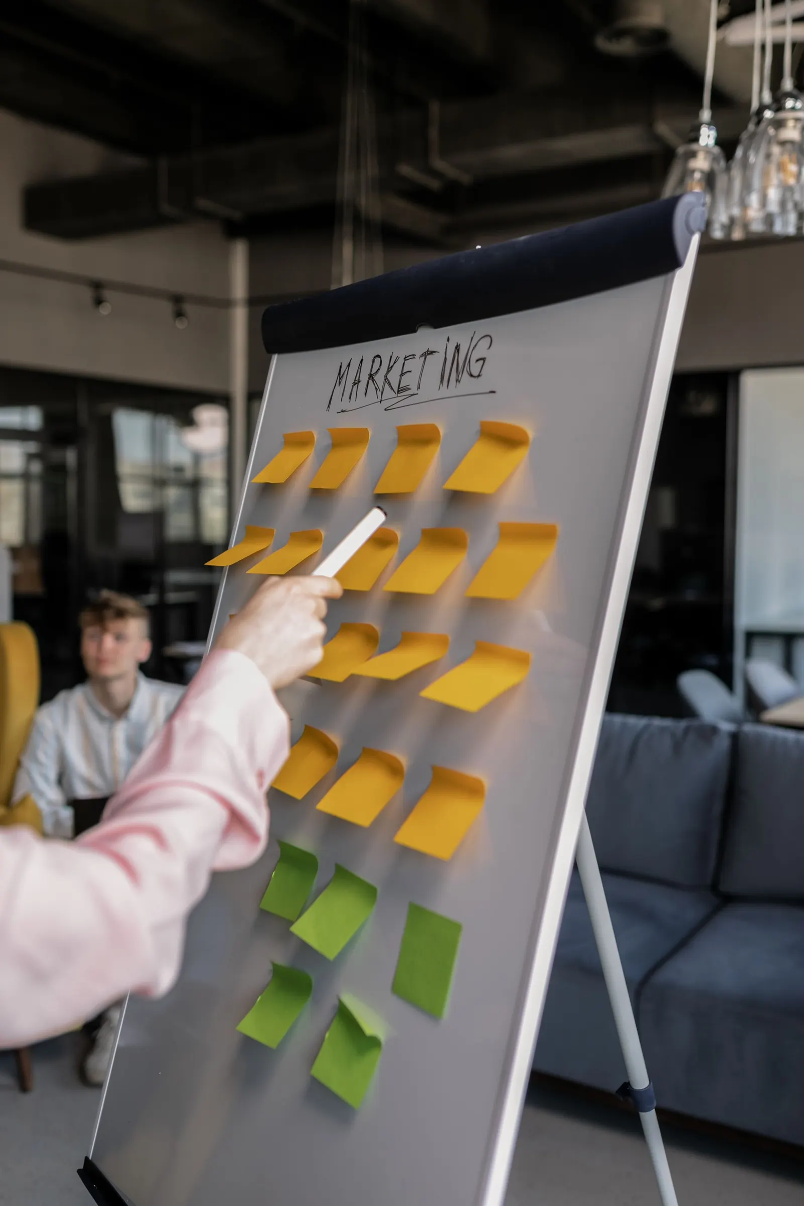 Person zeigt im Strategie-Workshop auf ein Whiteboard mit gelben Haftnotizen und der Überschrift Marketing