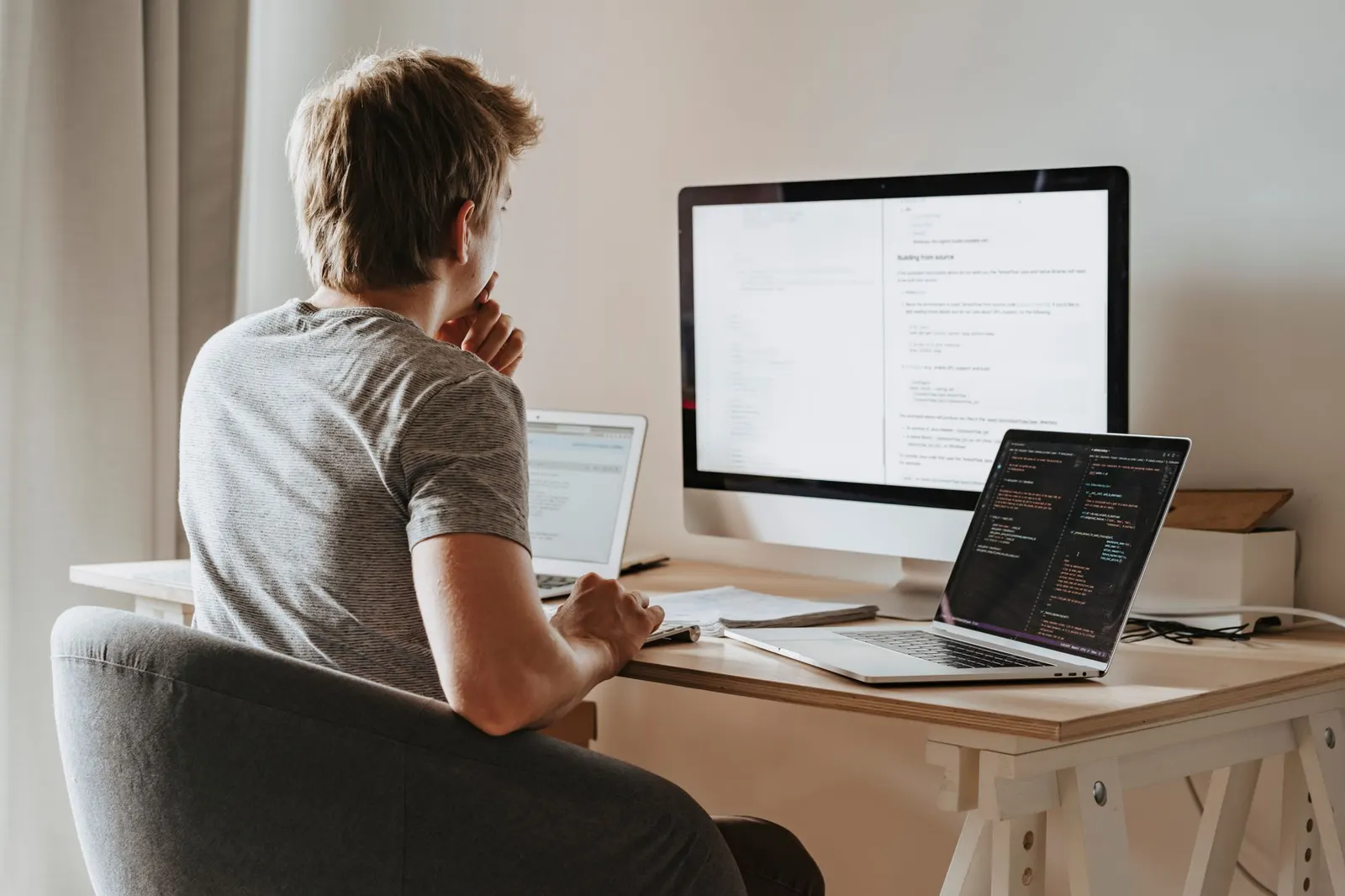 Mann sitzt vor einem Monitor und einem Laptop und analysiert Inhalte einer Website